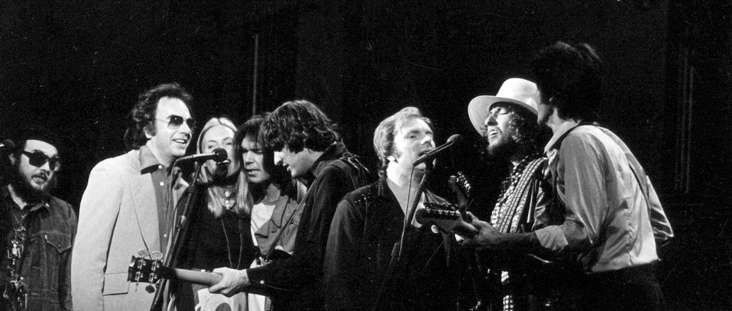 Schwarz-weiss-Fotografie einer Gruppe von Musikerinnen und Musikern auf der Bühne während eines gemeinsamen Auftritts; mehrere stehen dicht am Mikrofon, teils mit Gitarren, in konzentrierter, festlicher Stimmung – eine Szene aus dem Konzert The Last Waltz im Winterland Ballroom, San Francisco, 1976.