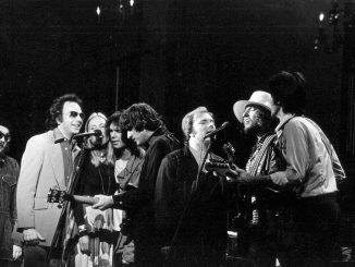 Schwarz-weiss-Fotografie einer Gruppe von Musikerinnen und Musikern auf der Bühne während eines gemeinsamen Auftritts; mehrere stehen dicht am Mikrofon, teils mit Gitarren, in konzentrierter, festlicher Stimmung – eine Szene aus dem Konzert The Last Waltz im Winterland Ballroom, San Francisco, 1976.