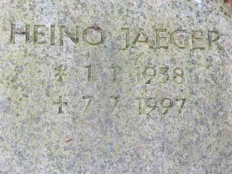 Grabstein aus grauem Granit mit der eingravierten Inschrift HEINO JAEGER * 1.1.1938 † 7.7.1997, umgeben von Laub auf dem Boden.