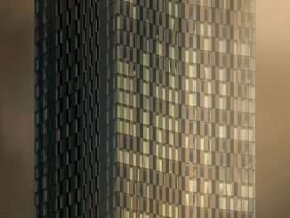 Hochhausfassade mit vielen kleinen Fensterquadraten, teilweise reflektierend in warmen Gold- und Bronzetönen, vom unteren Bildrand her aufsteigender dichter Nebel oder Dampf, der das Gebäude halb verdeckt; Stimmung düster-mystisch.